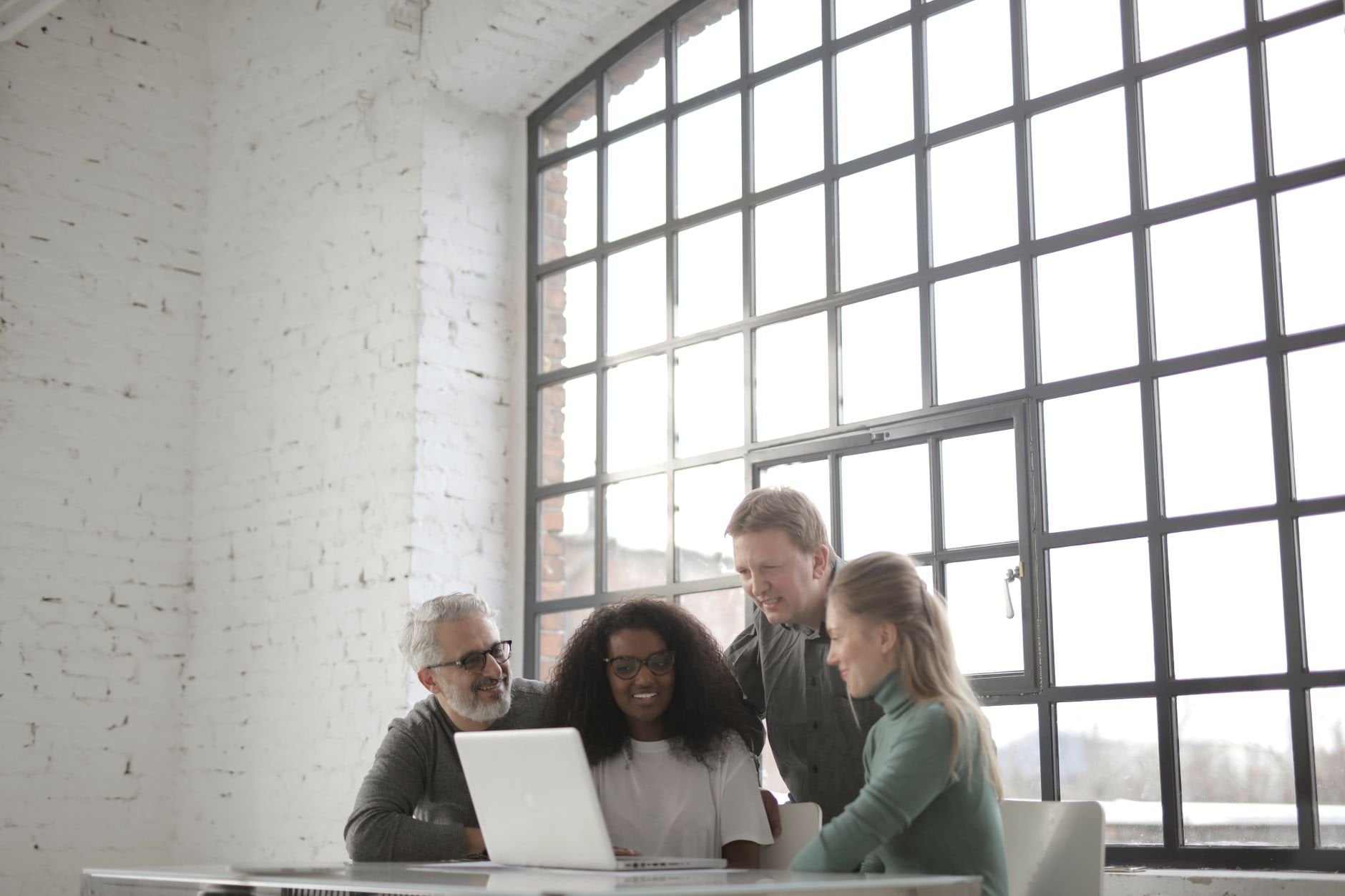Positive focused multiracial coworkers collaborating near a table with a laptop in a modern workplace.